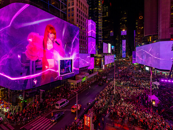 Pink-lit LED screens showing the Fortnite Remix performer tower over a Times Square crowd at night