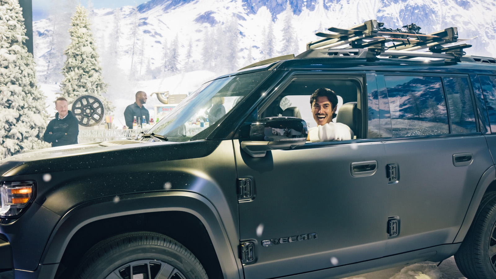 Man grinning inside a Jeep Recon at a snowy alpine brand activation set