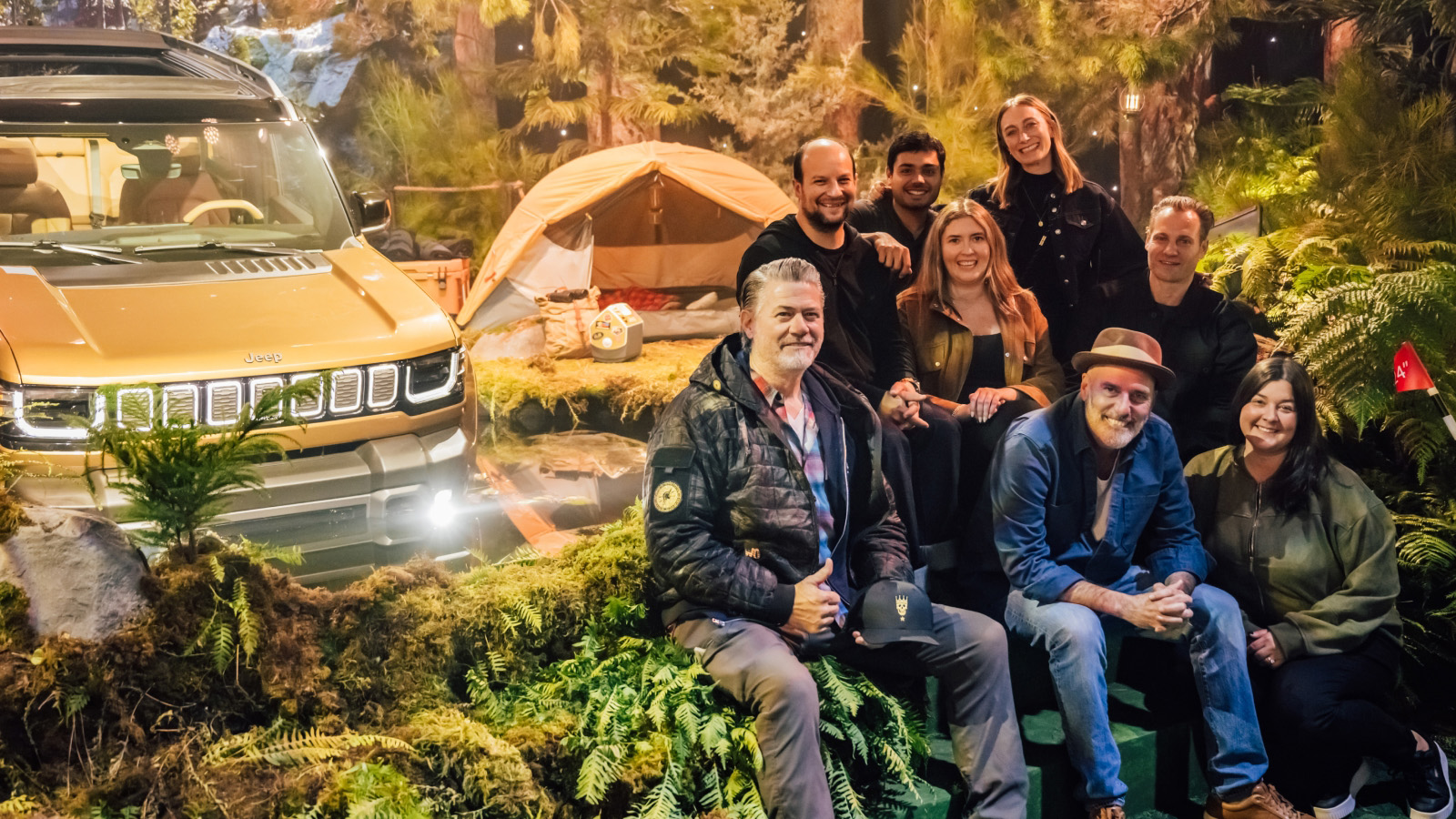 Team seated with a gold Jeep and glamping tent inside an immersive forest brand set