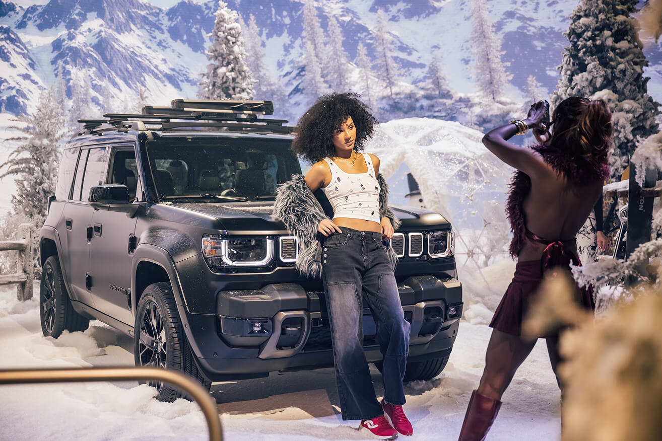 Model posing beside a matte black Jeep in a snowy alpine experiential set