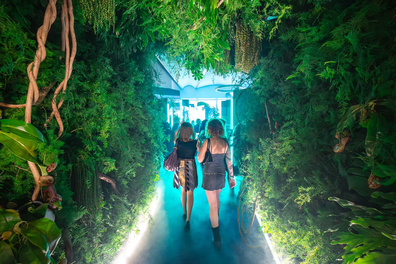 Guests walk a lush jungle-themed corridor with hanging plants and teal haze at an experiential brand activation