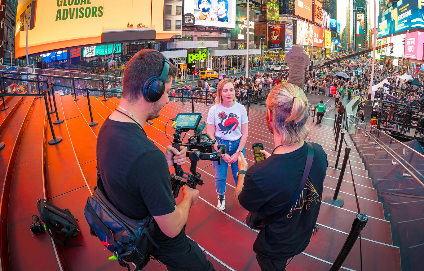 Camera crew filming a presenter on the red steps of Times Square, New York