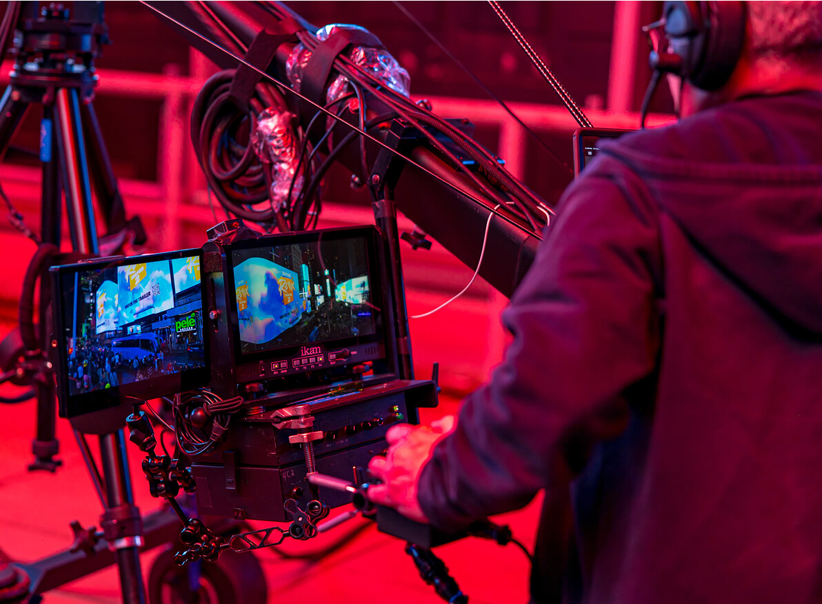 Camera operator on a jib rig monitoring Times Square footage under red lighting
