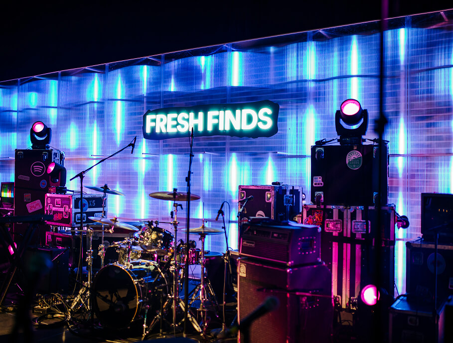 Drum kit and road cases against glowing Fresh Finds neon and pixel backdrop at Spotify stage