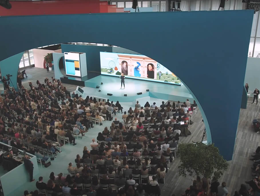 Aerial view of packed audience facing arched stage and video wall at LinkedIn B2Believe