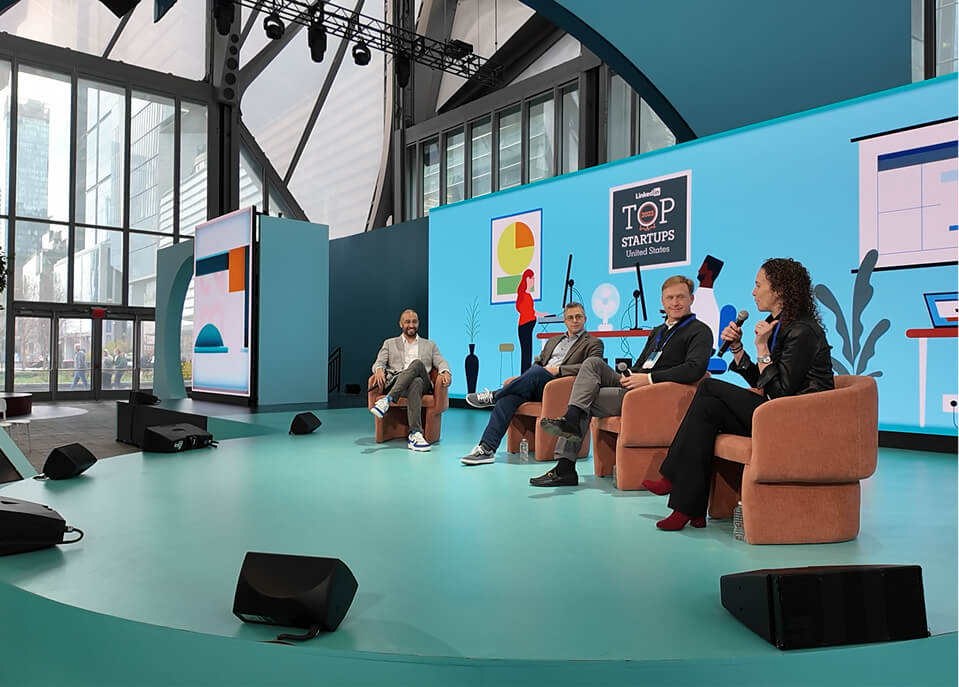 Panel of four seated on stage before Top Startups screen at LinkedIn B2Believe