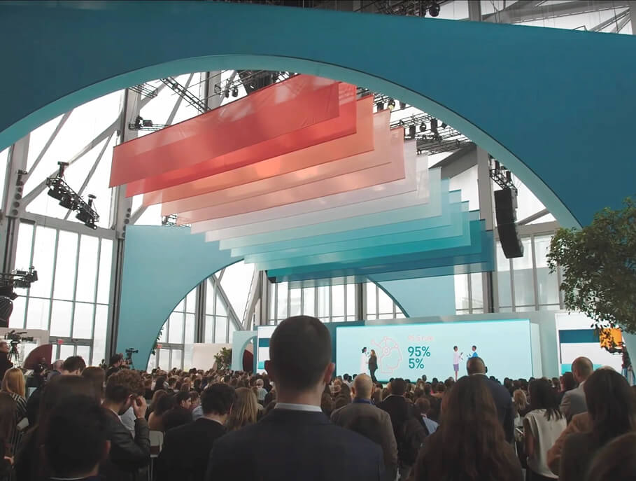 Standing crowd watches speakers under suspended color panels at LinkedIn B2Believe finale