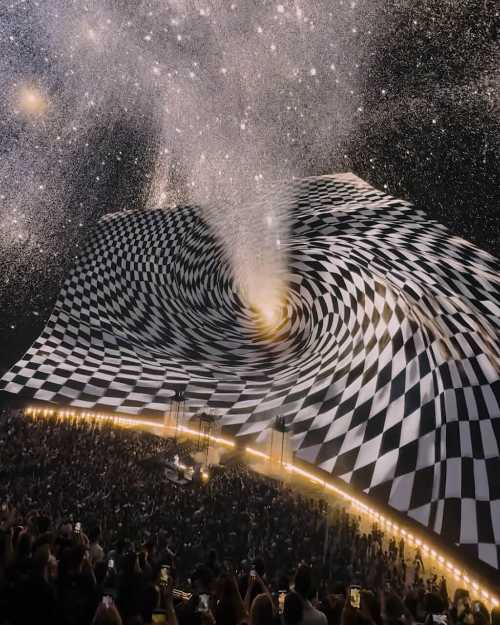 Swirling black-and-white checkerboard vortex on The Sphere dome above phone-lit John Summit crowd