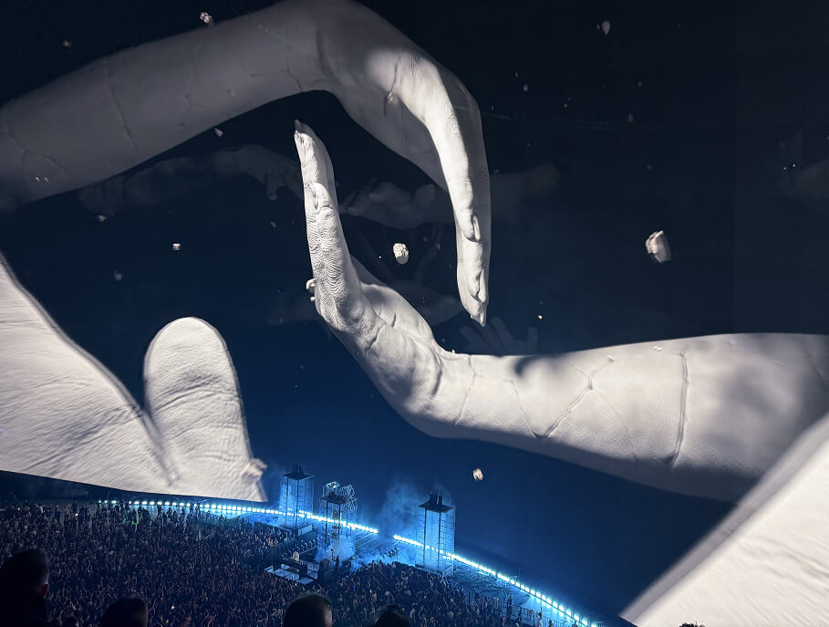Huge white sculptural hands projected over the arena stage at The Sphere
