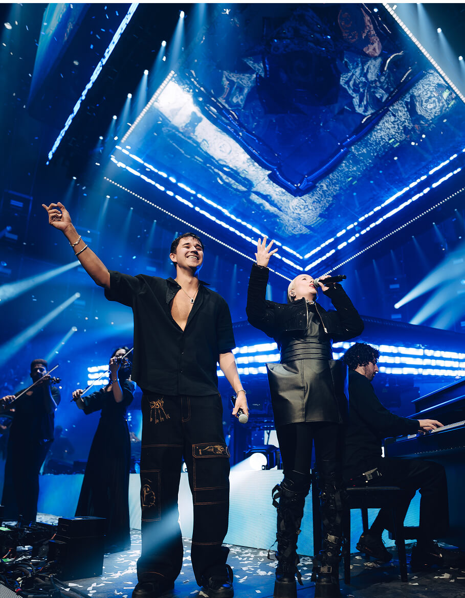 John Summit and a singer take a bow with strings and pianist under blue lights