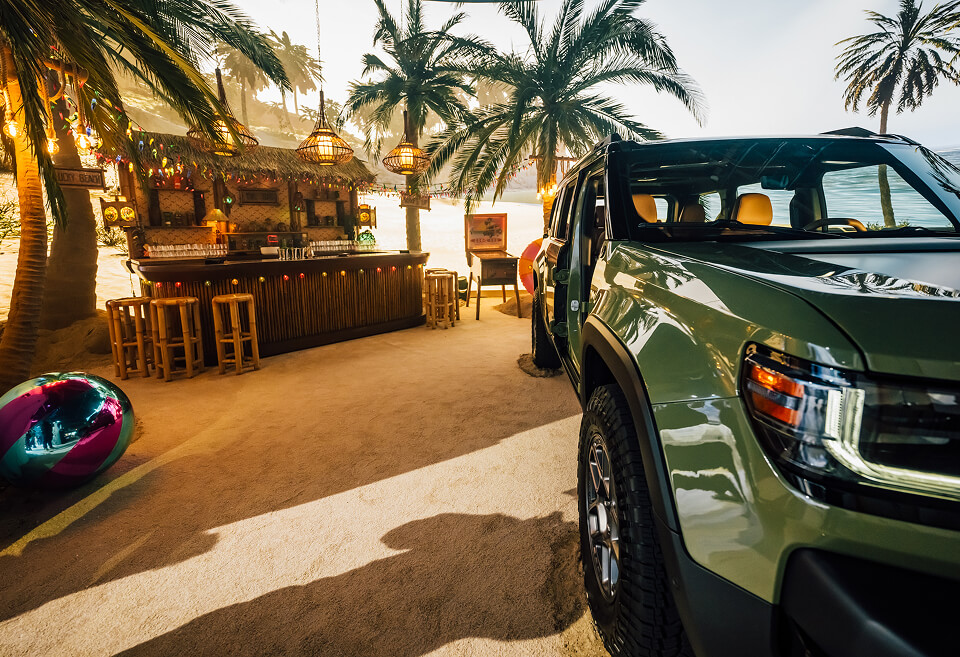 Green Jeep Recon parked by a tiki beach bar under palm trees at the reveal event