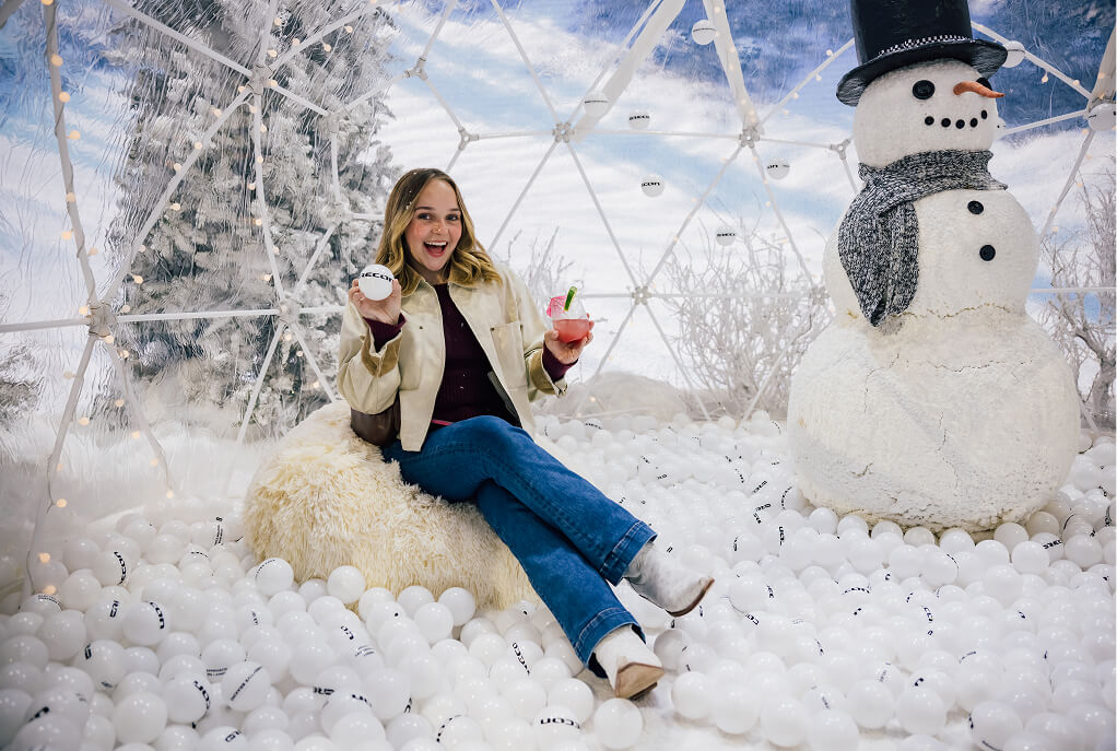 Guest sits in a snow-globe ball pit beside a snowman at the Jeep Recon reveal