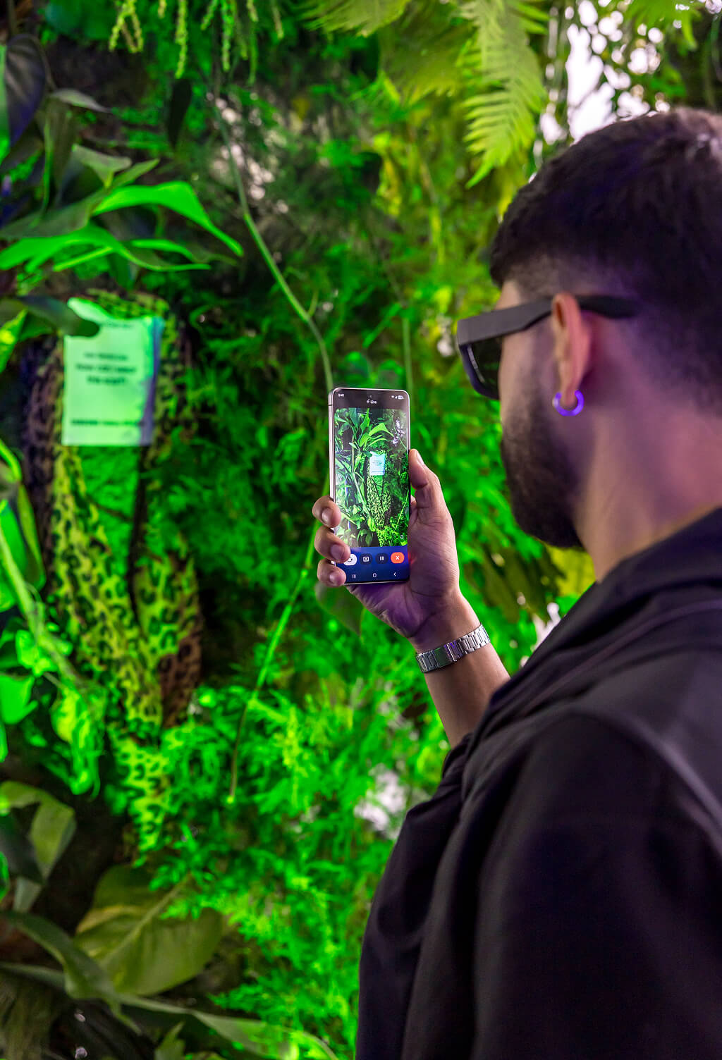 Guest in sunglasses filming a lush green jungle plant wall on a Samsung Galaxy S25 Edge