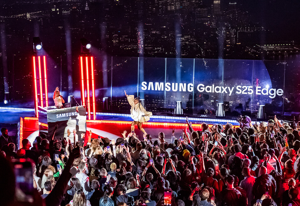 Rooftop crowd raising phones as a performer takes the Samsung Galaxy S25 Edge launch stage over the NYC skyline