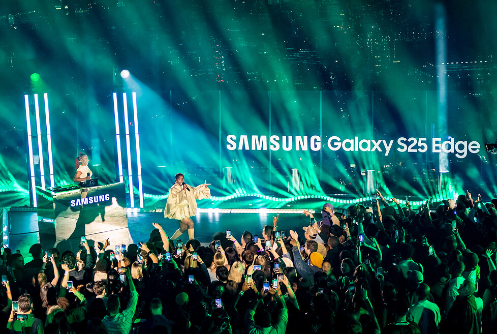 Green laser fan behind the Samsung Galaxy S25 Edge stage as fans film the performer with phones
