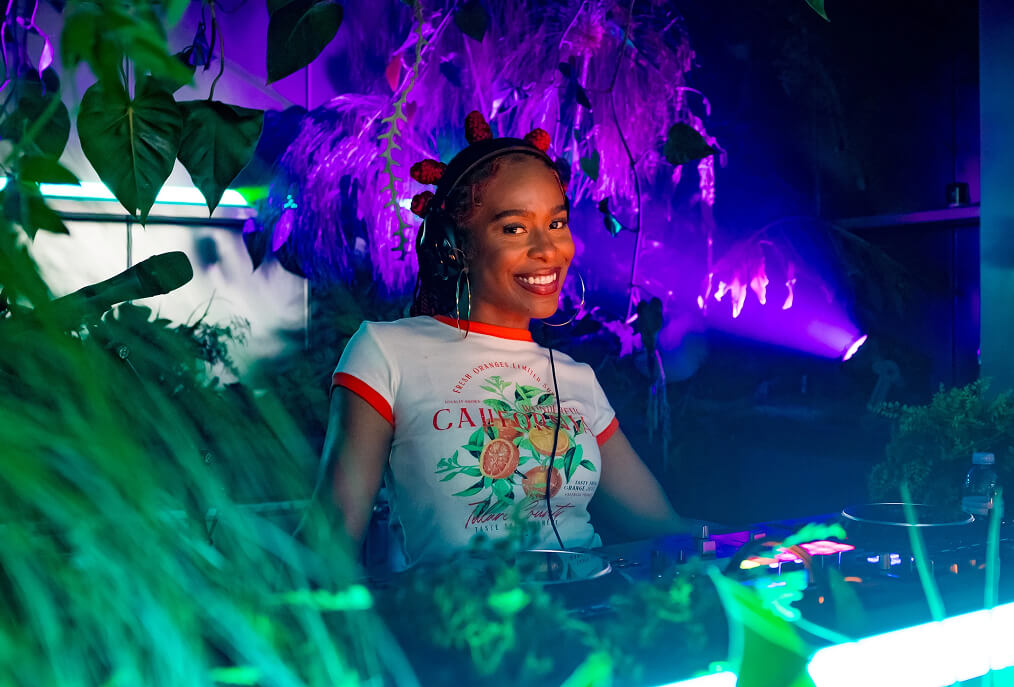 Smiling DJ in headphones spinning amid neon-lit tropical plants at the Samsung Galaxy S25 Edge event