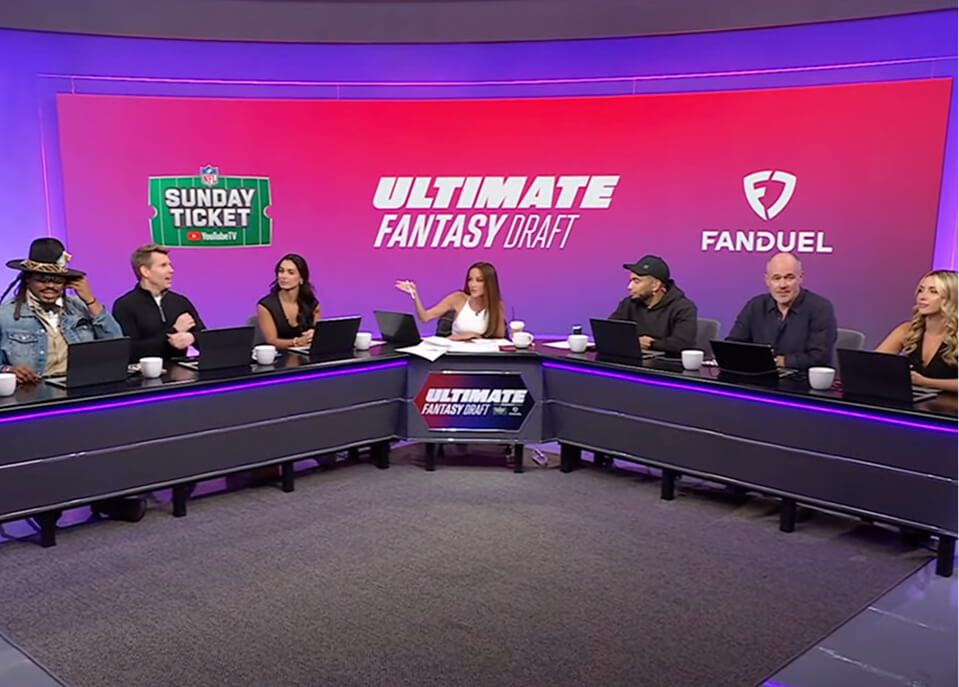 Panel of hosts and NFL talent at the Ultimate Fantasy Draft studio desk under a magenta LED wall