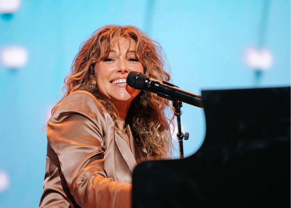 Singer smiling at the mic while playing grand piano at the Susan Wojcicki Foundation Gala