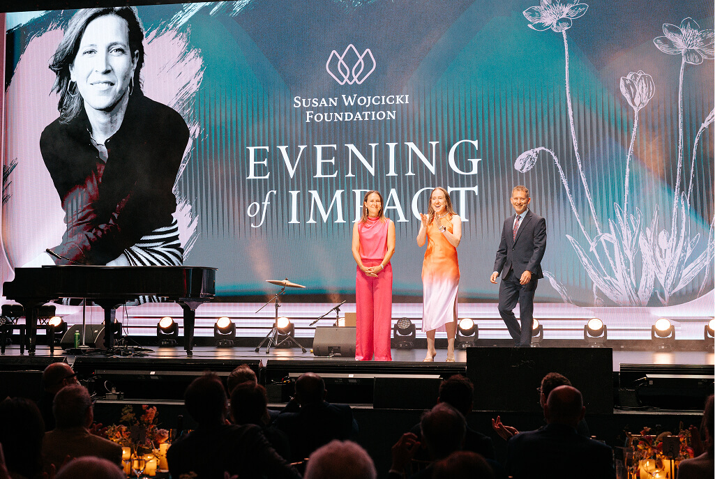 Three speakers on stage before the Evening of Impact LED screen at the Wojcicki Foundation Gala