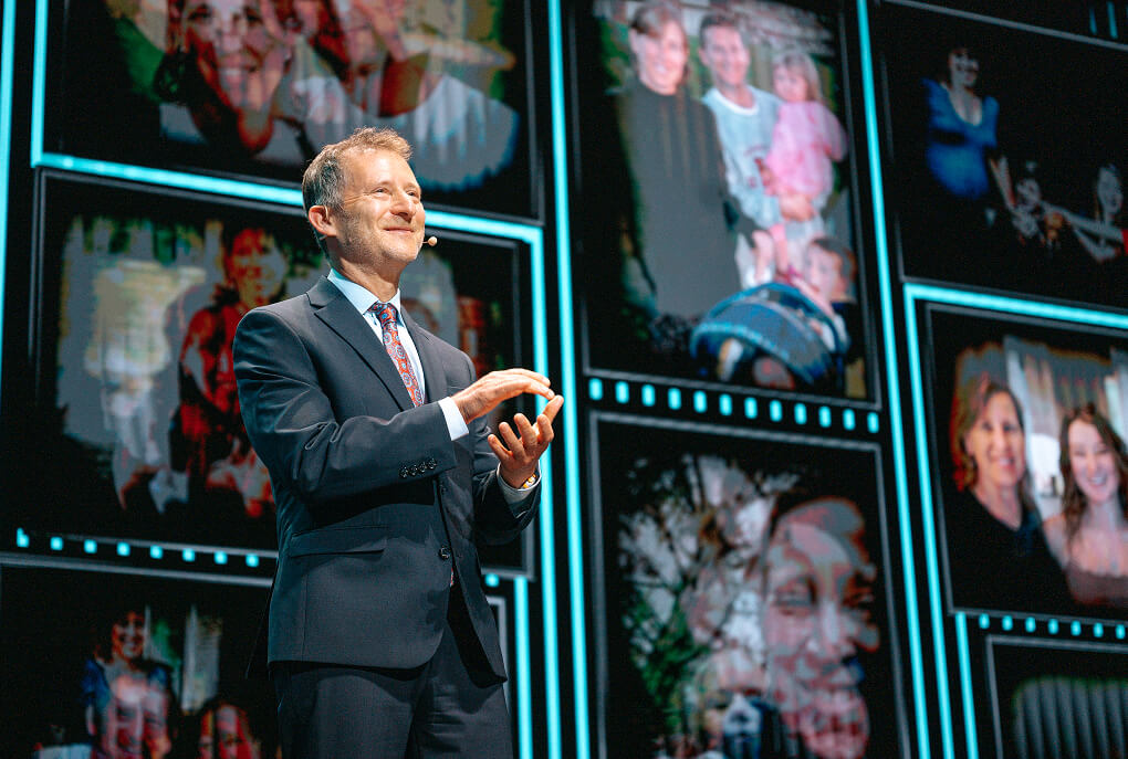 Speaker in a suit before a video wall of family photos at the Wojcicki Foundation Gala