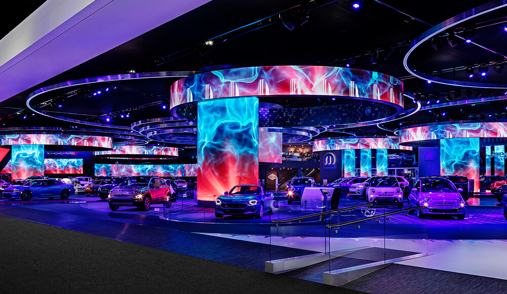 Auto show floor with cars circled by curved LED rings and blue flame content on screens