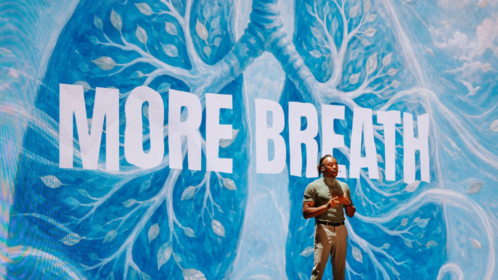 Speaker on stage with 'More Breath' blue lung tree backdrop